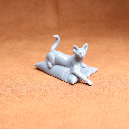 White cat figurine lying on a pillow against an orange background