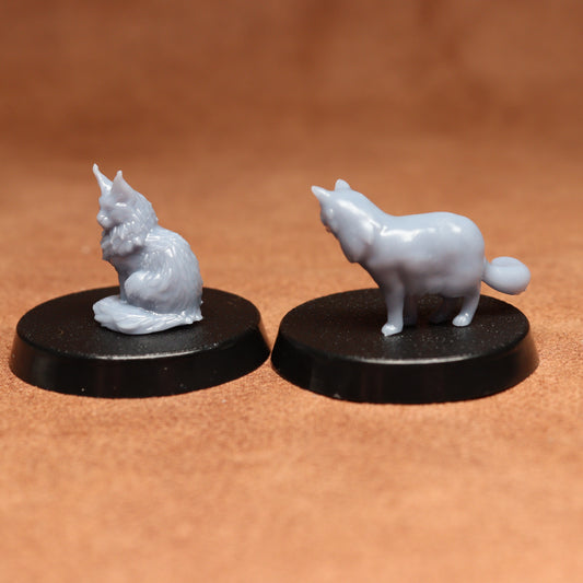 Two miniature figurines of a cat and a cat on black bases against a brown background