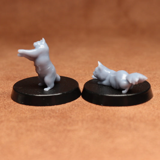 Two miniature bear cat figurines on black bases against a brown background