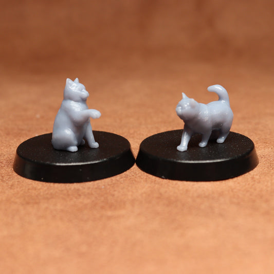 Two miniature cat figurines on black bases against a brown background