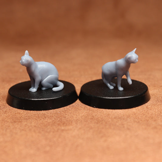 Two miniature cat figurines on black bases against a brown background