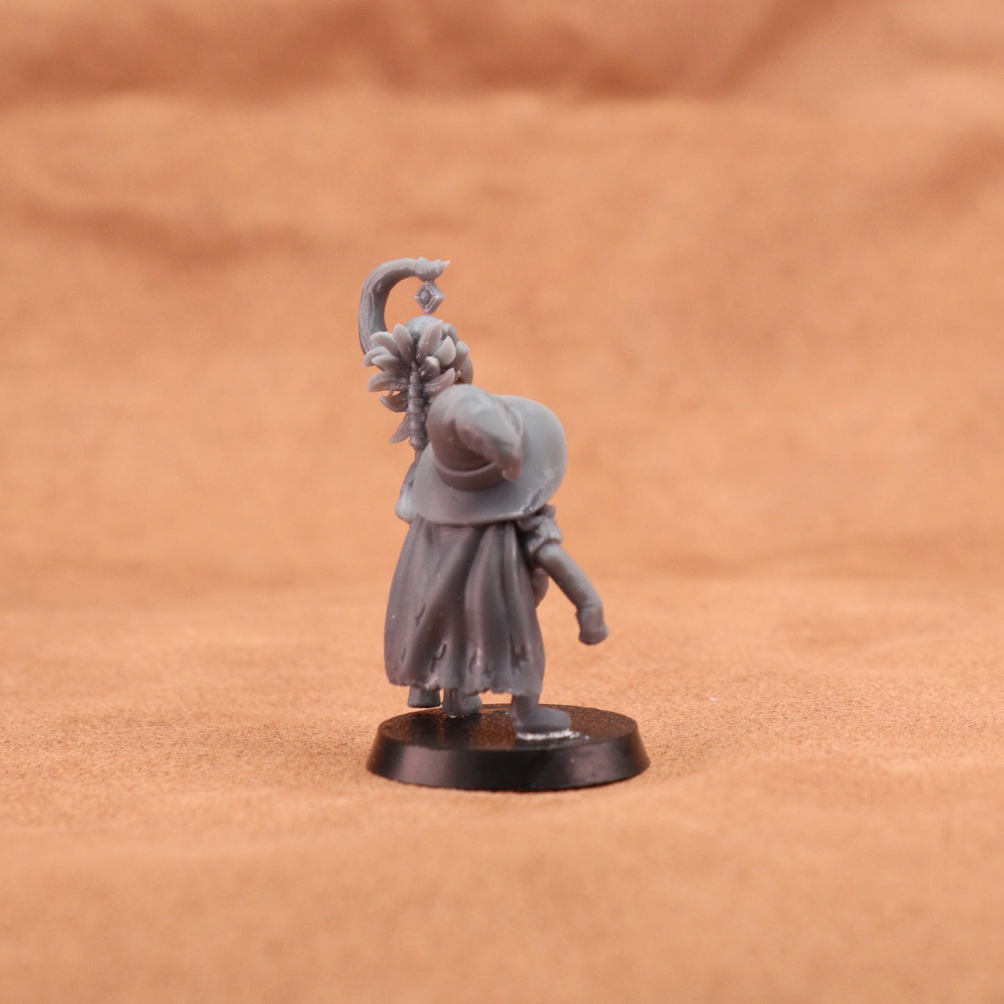 An unpainted grey fantasy miniature figurine of a woman with a curved sword, standing on a black circular base against a textured brown background.