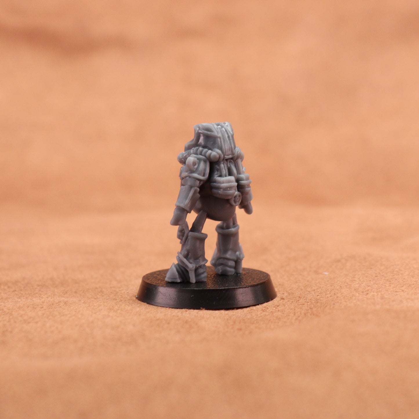 A small gray sci-fi miniature figurine standing on a round black base, photographed against a warm tan textured background.