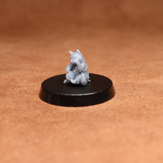 grey resin miniature cat figure on a black base with a brown background