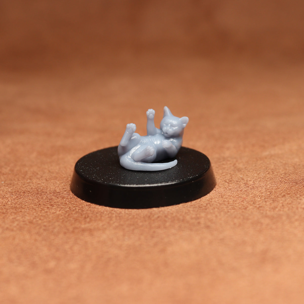 a grey cat figurine laying on its back on a black base on a brown background