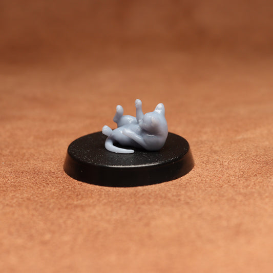 Small figurine of a cat lying on their back on a black base against a brown background