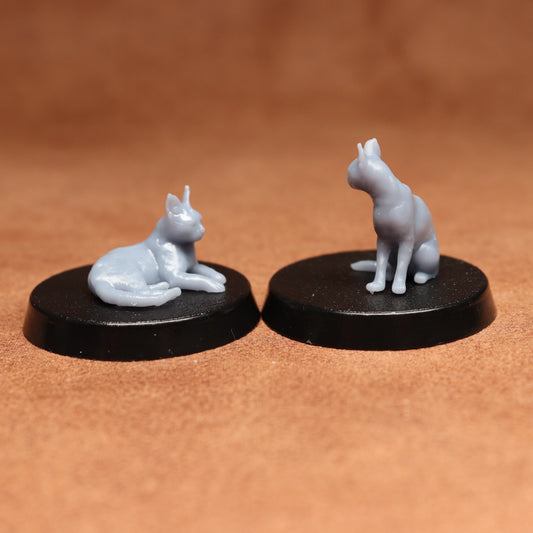 Two miniature cat figurines on black bases against a brown background