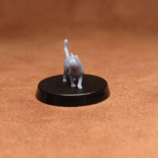 Small gray cat figurine on a black round base against a brown background