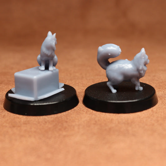 Two miniature cat figurines on black bases against a brown background