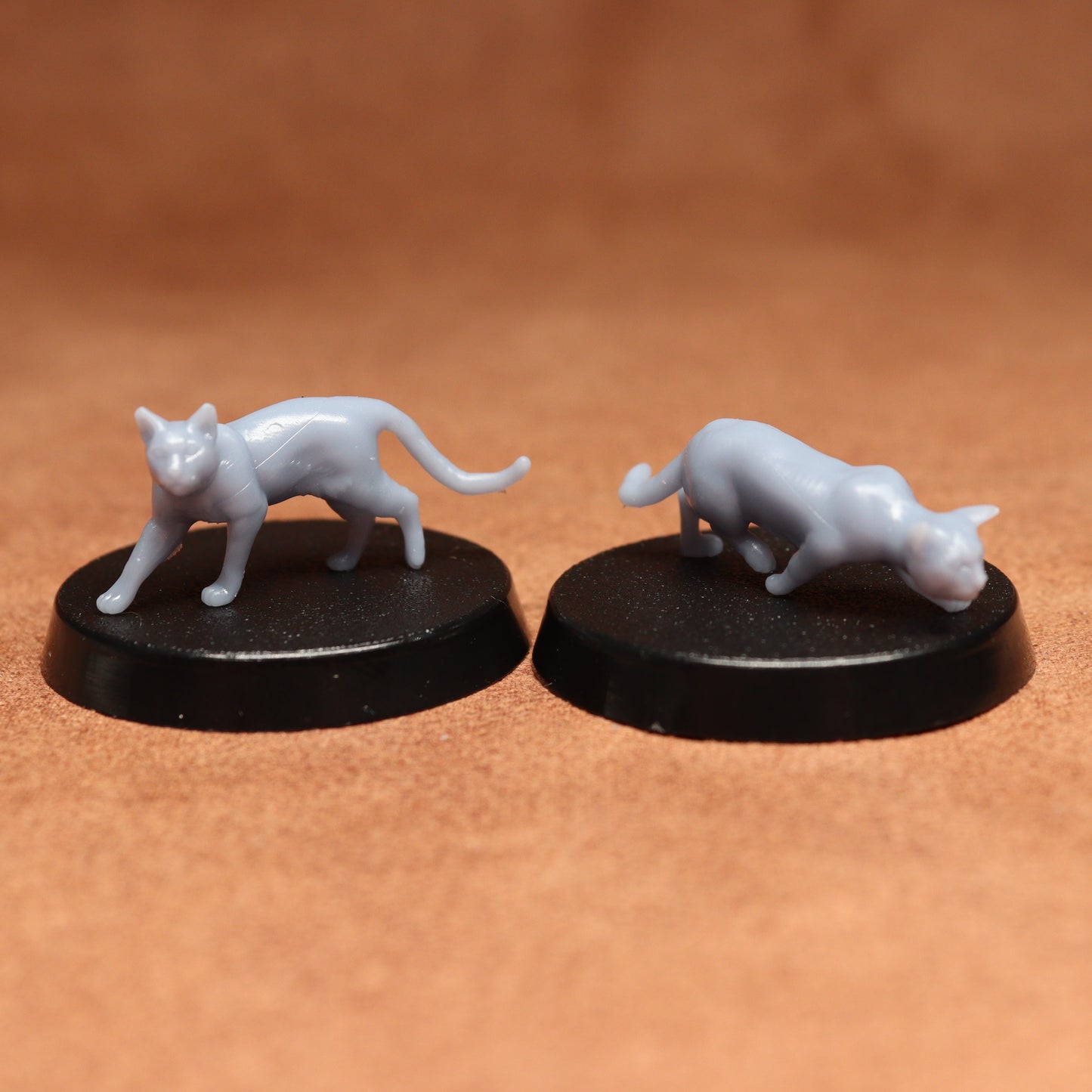 Two miniature cat figurines on black bases against a brown background