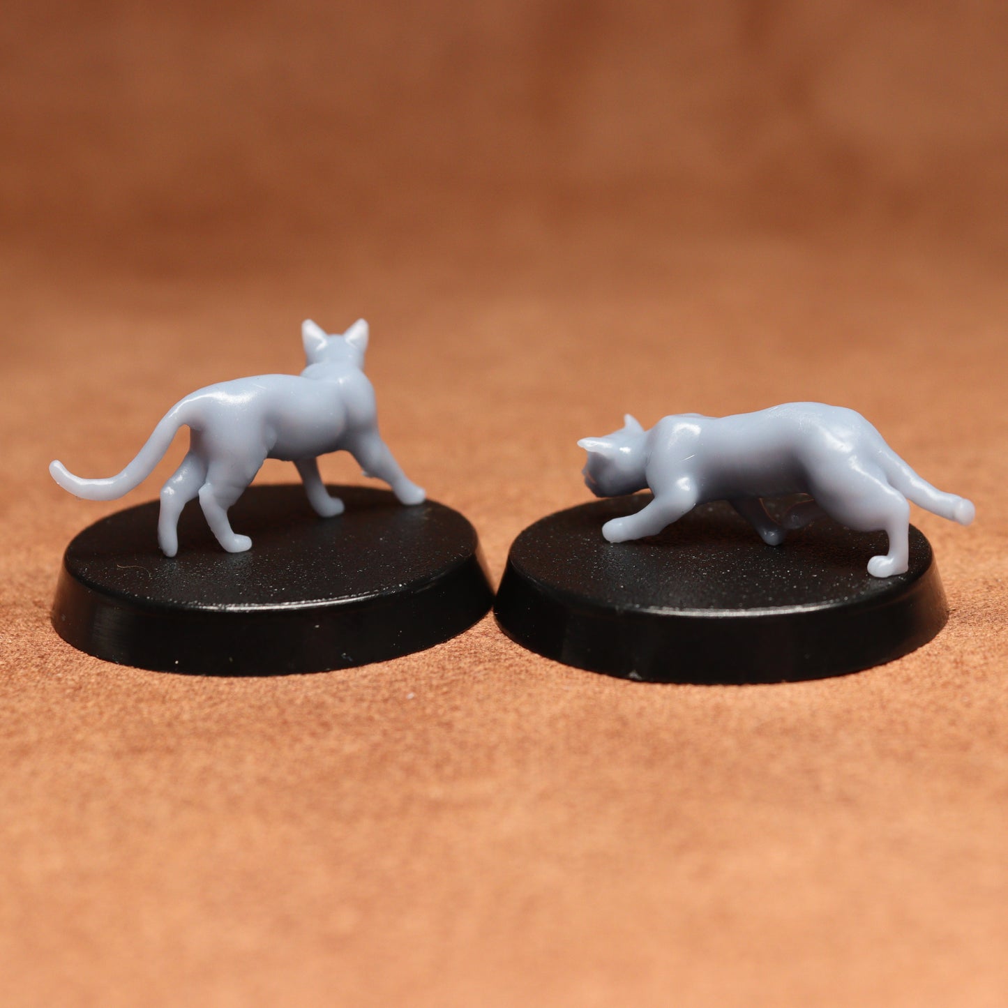Two white cat figurines on black bases against a brown background
