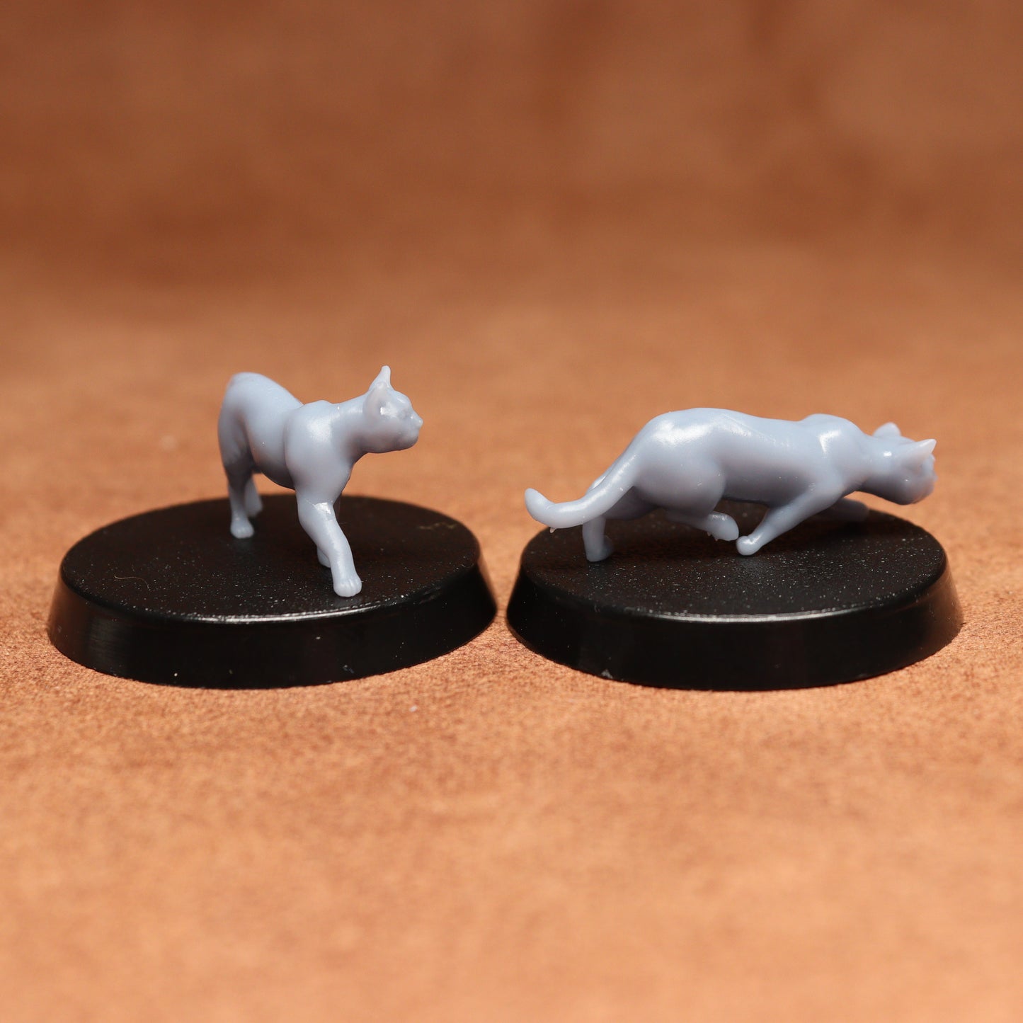 Two white cat figurines on black bases against a brown background