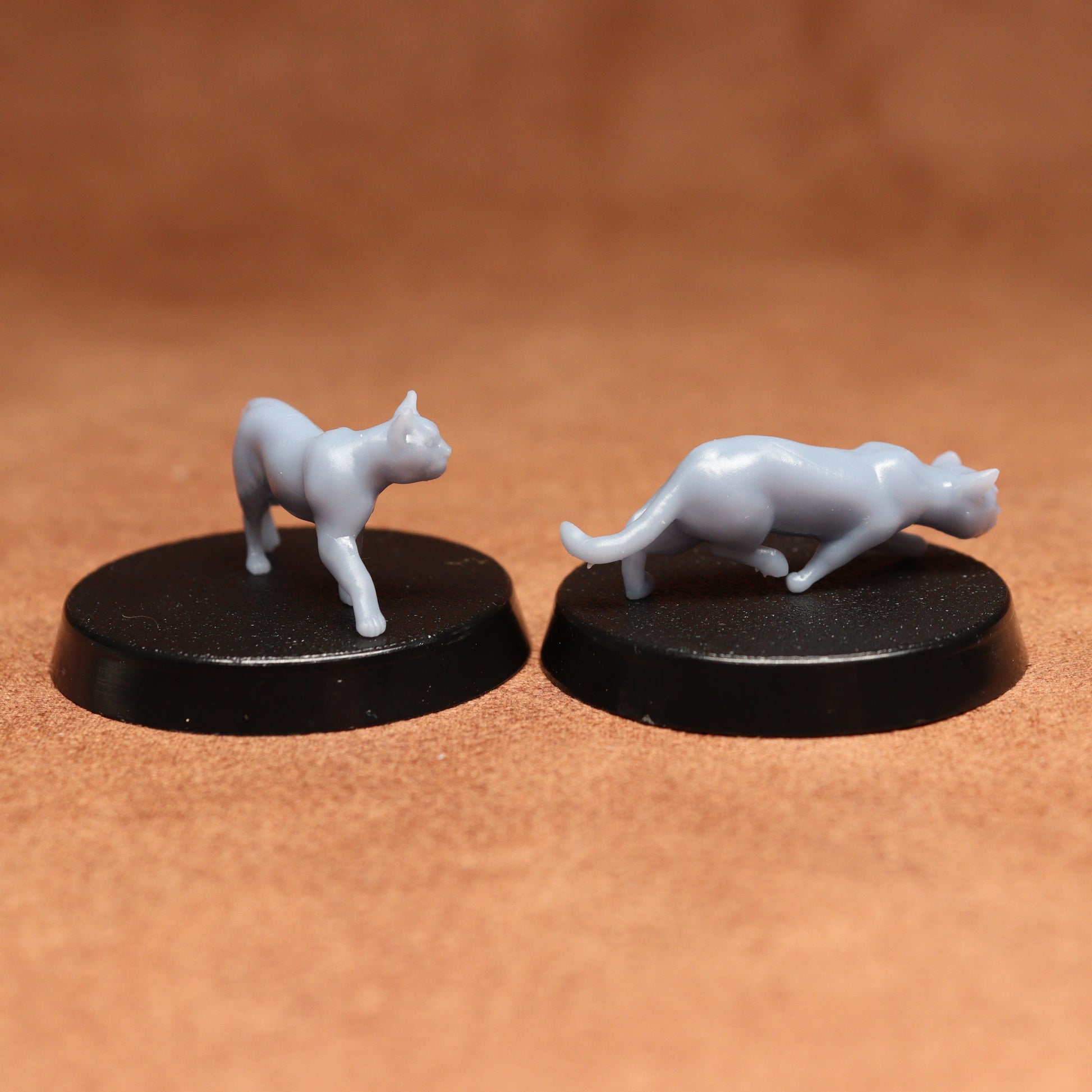 Two white cat figurines on black bases against a brown background
