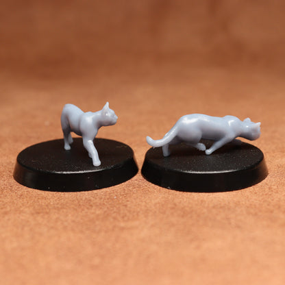 Two white cat figurines on black bases against a brown background