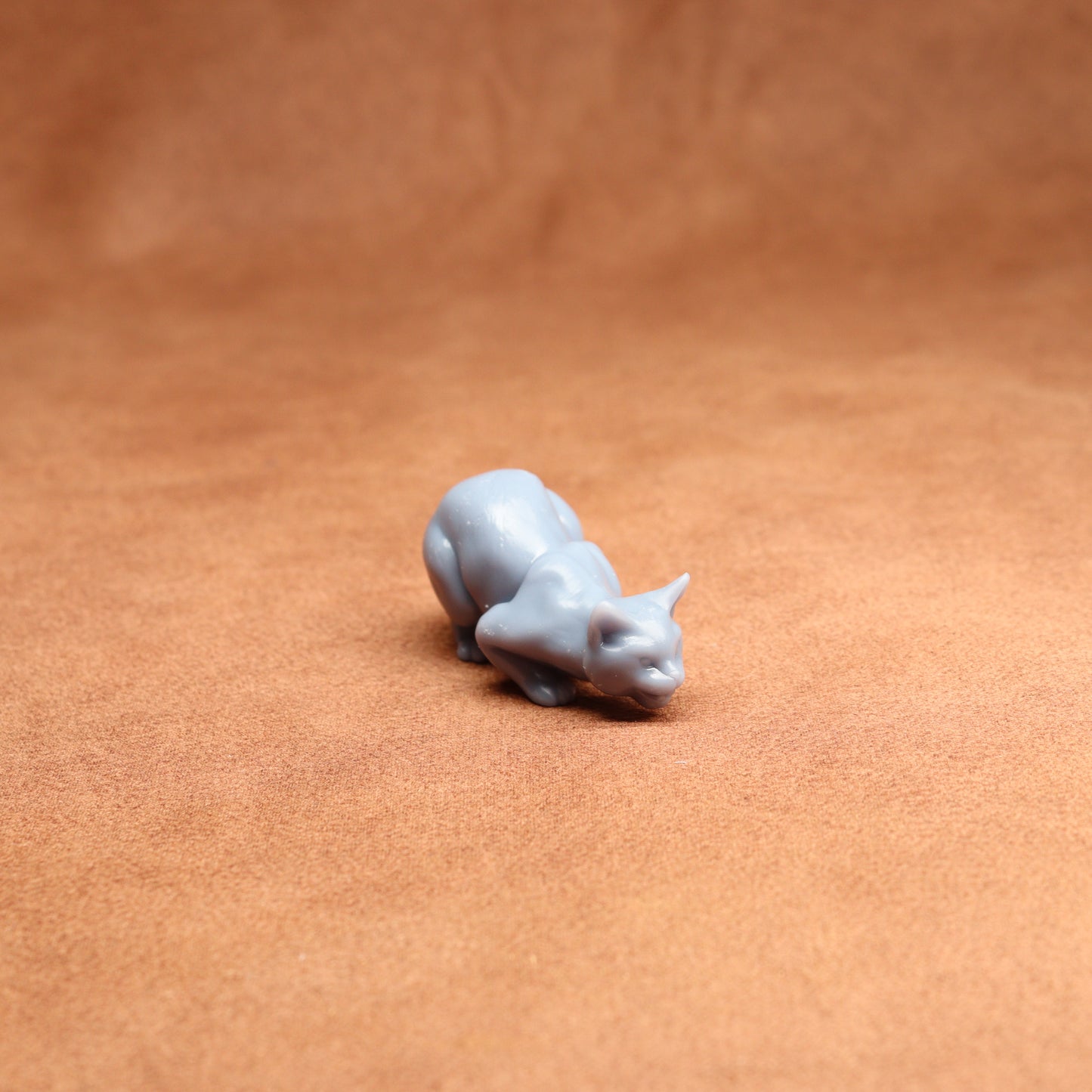 Small gray cat figurine on a brown leather surface
