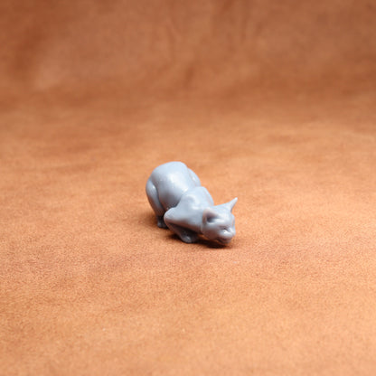 Small gray cat figurine on a brown leather surface
