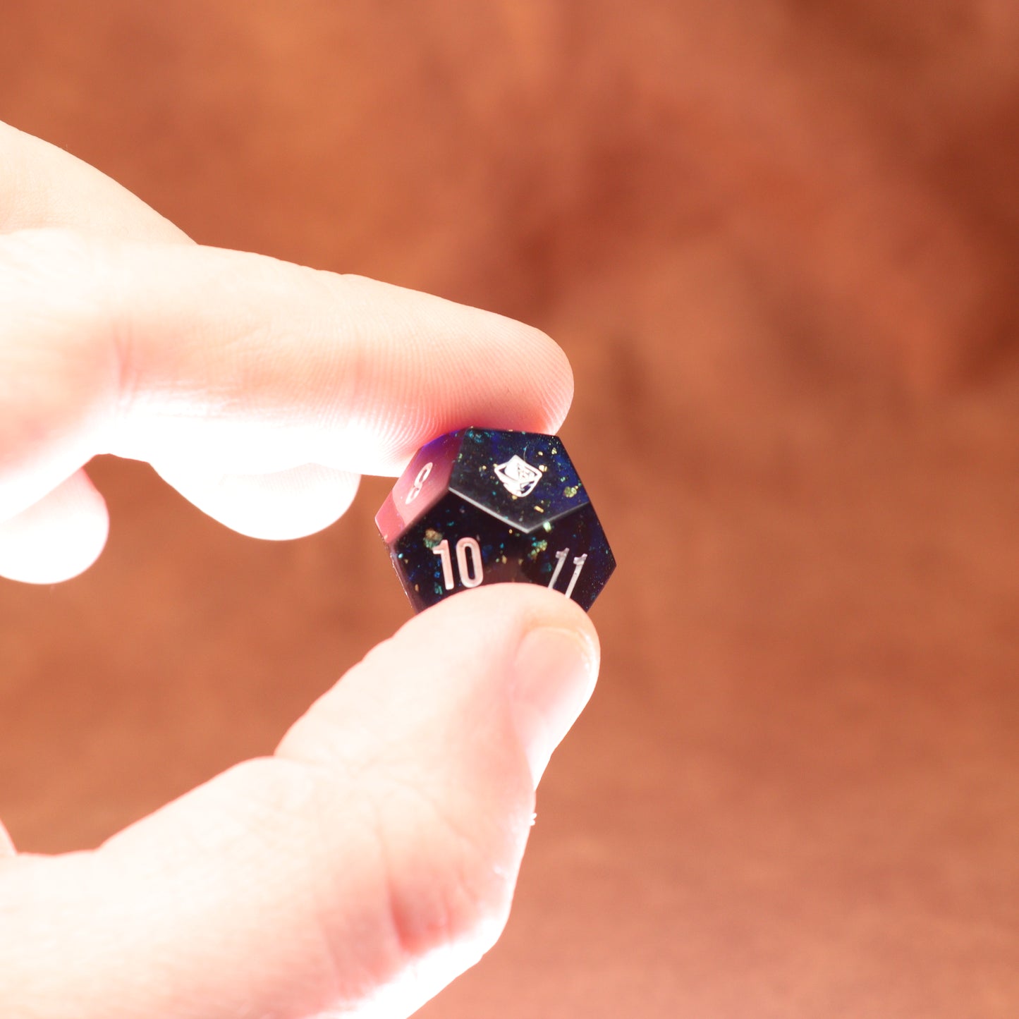 Hand holding a small polyhedral dice with numbers on a brown background