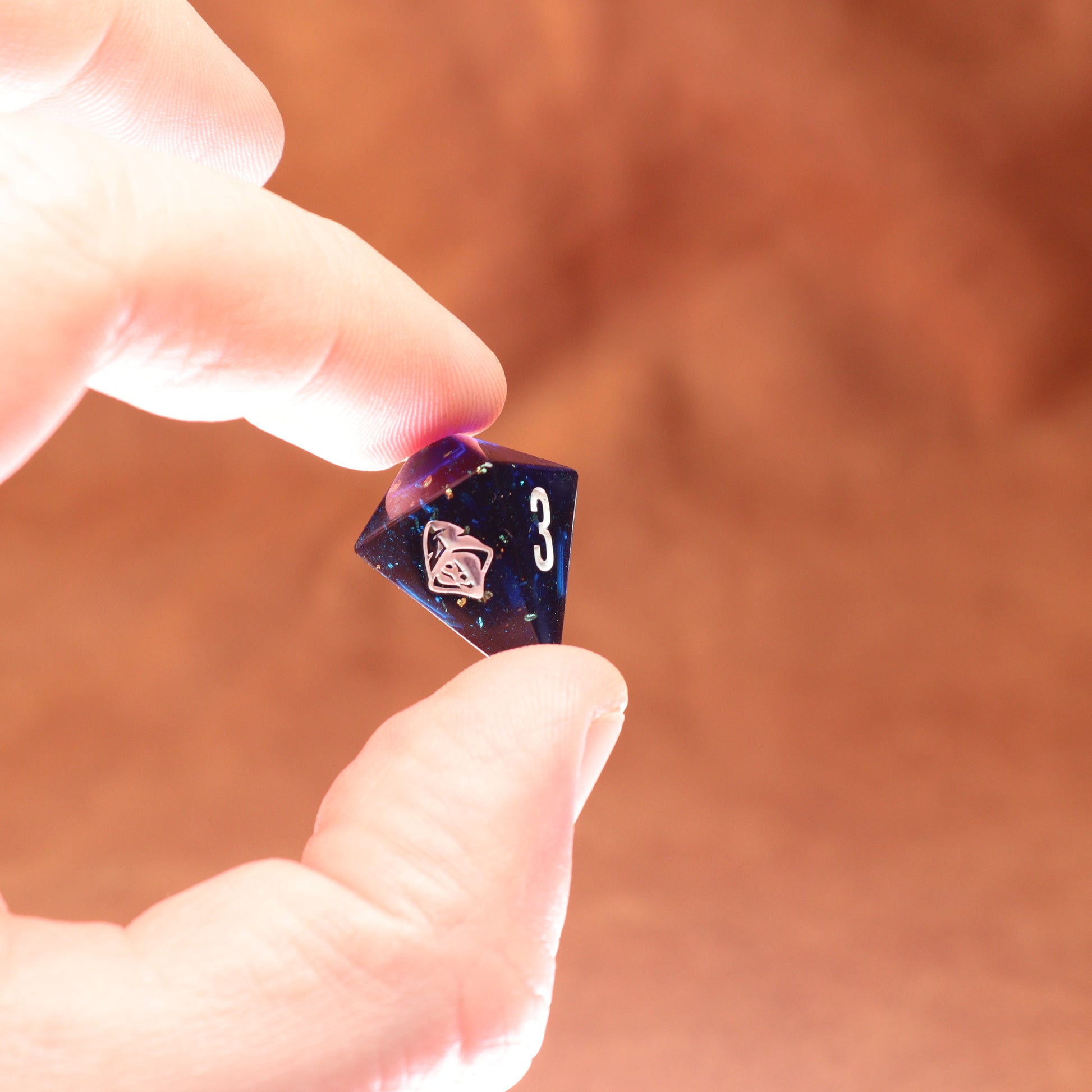 Hand holding a purple polyhedral dice with number 3 on a brown background