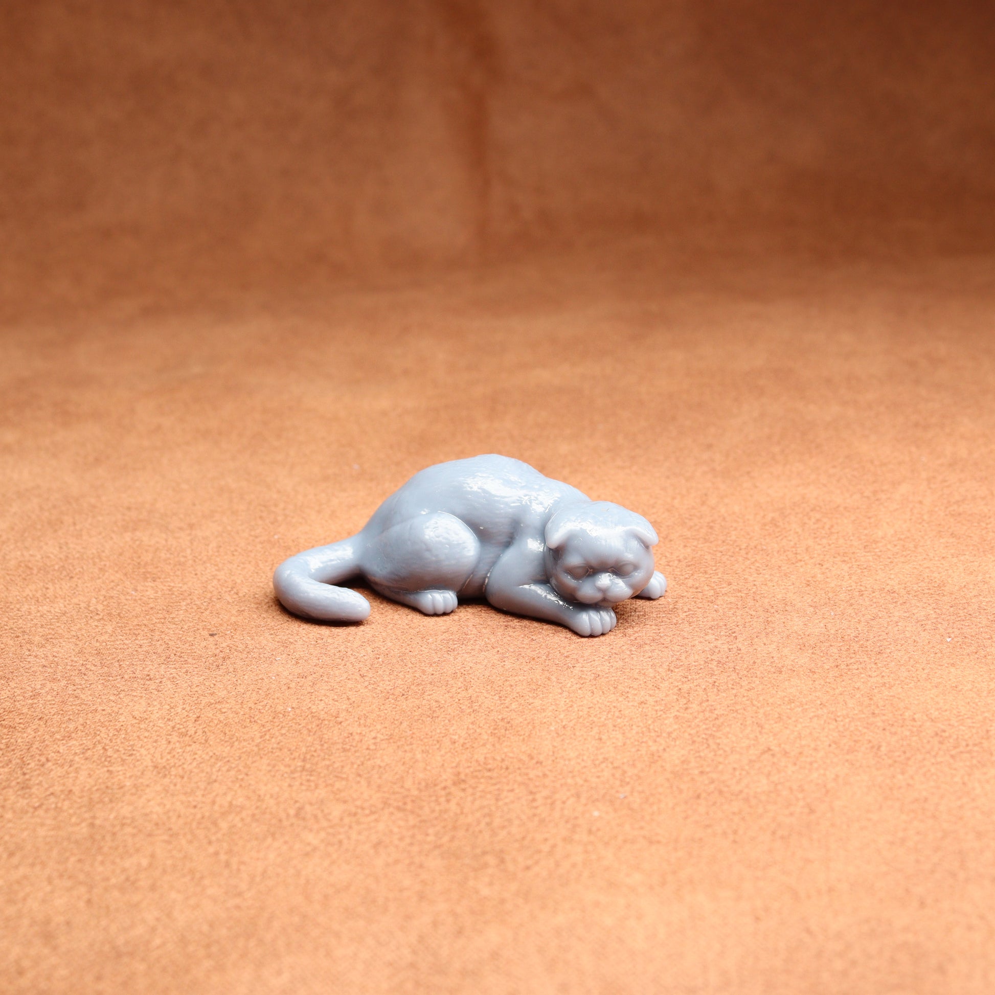 Small gray figurine of a cat on a brown surface