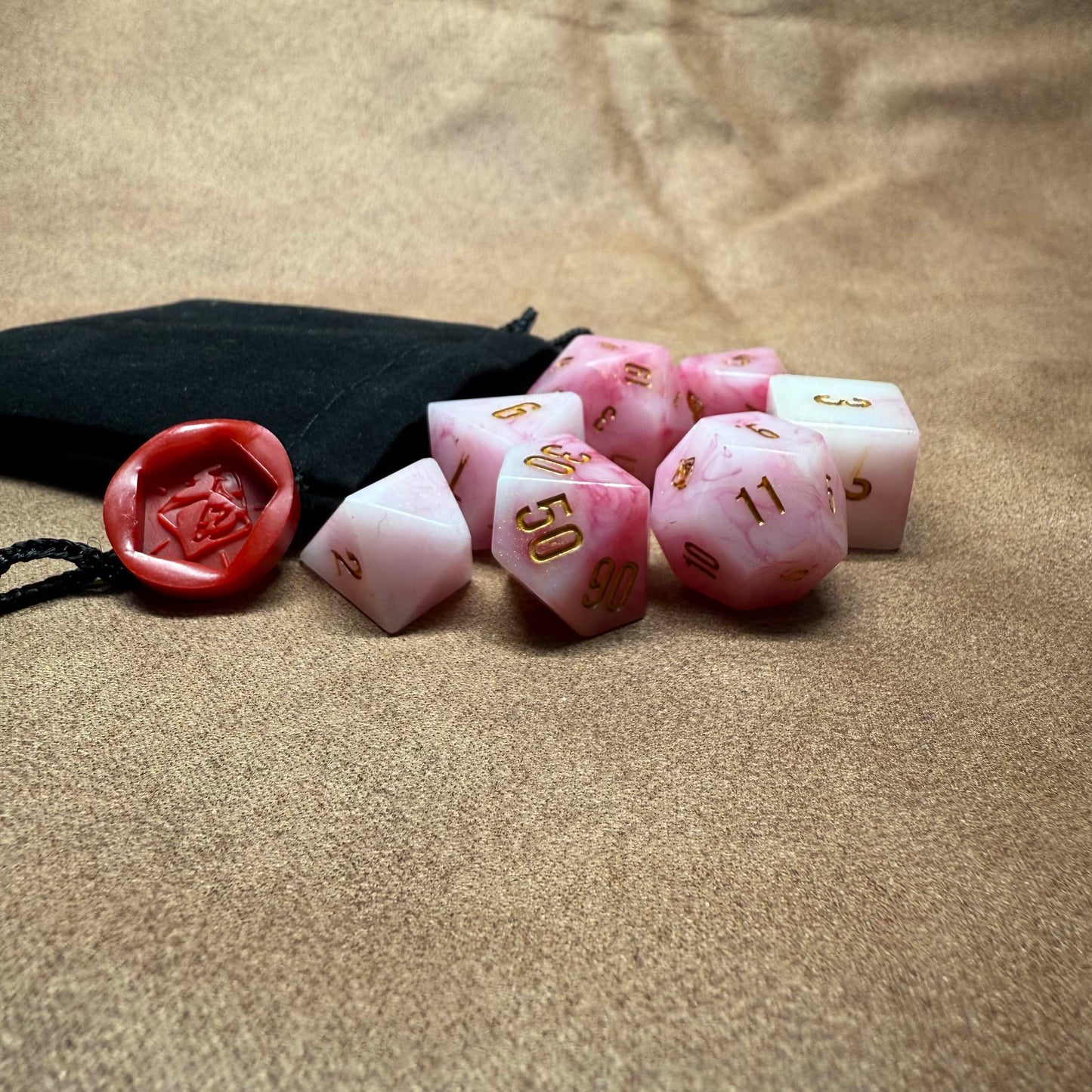 Pink polyhedral dice set with a black drawstring bag on a beige surface
