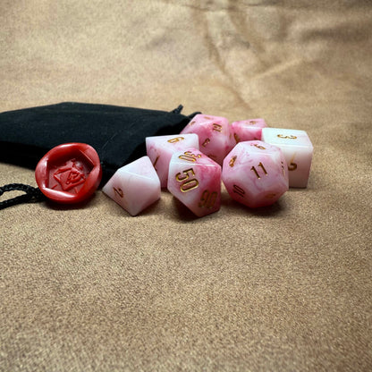 Pink polyhedral dice set with a black drawstring bag on a beige surface