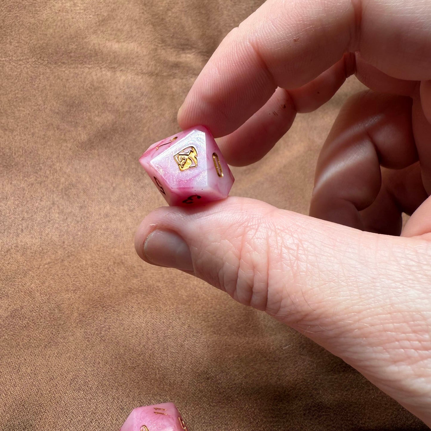 Hand holding a pink die with gold accents on a brown surface