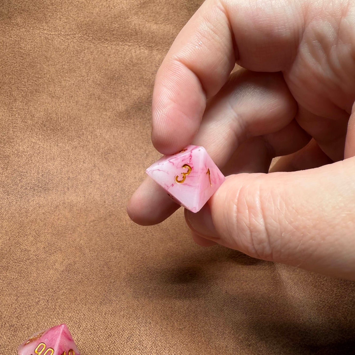 Hand holding a pink die with numbers on a brown surface