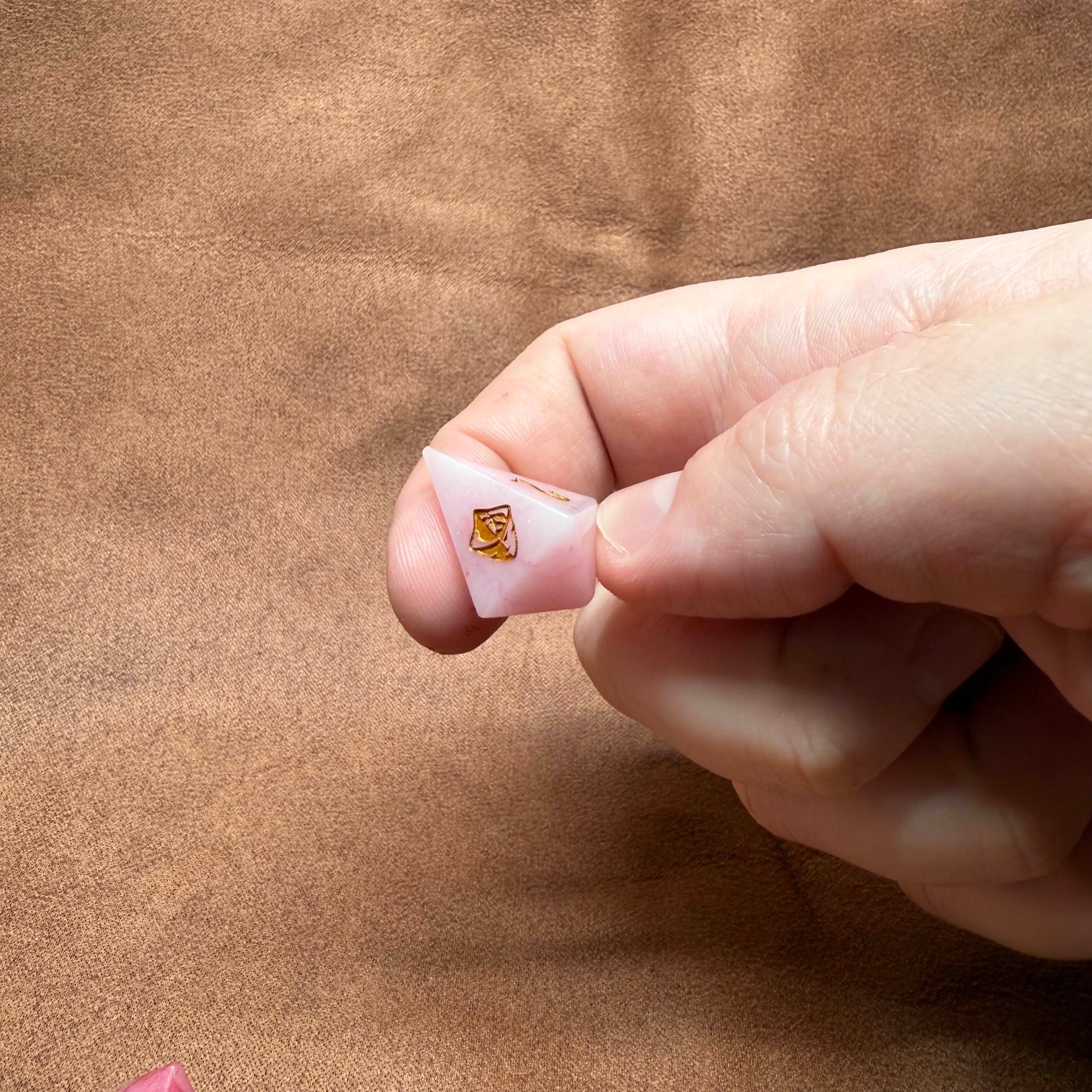 Hand holding a small pink object with a gold emblem on a brown background