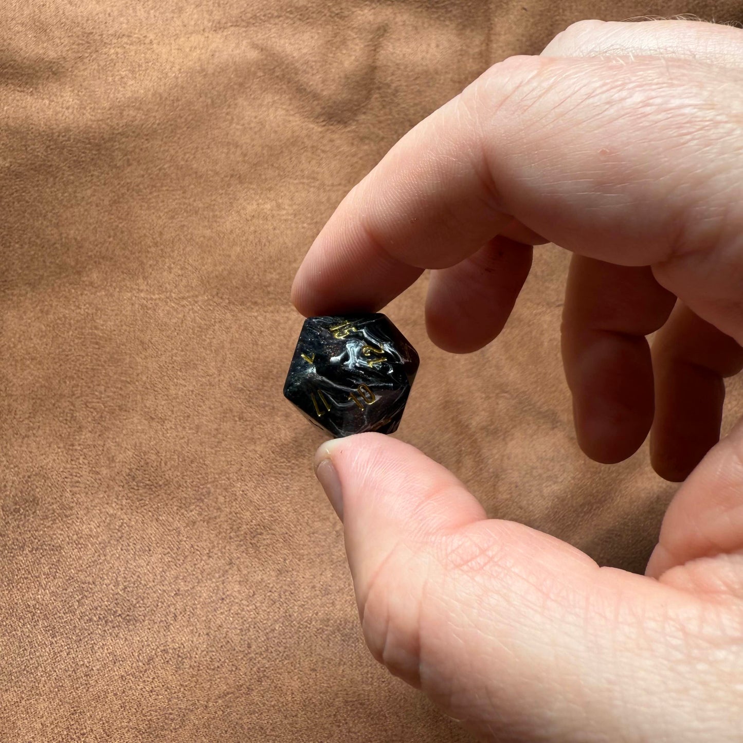 Hand holding a small black stone against a brown fabric background