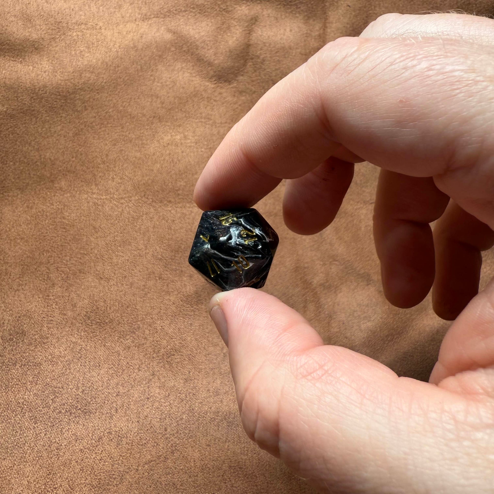 Hand holding a small black stone against a brown fabric background
