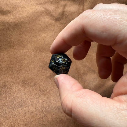 Hand holding a small black stone against a brown fabric background