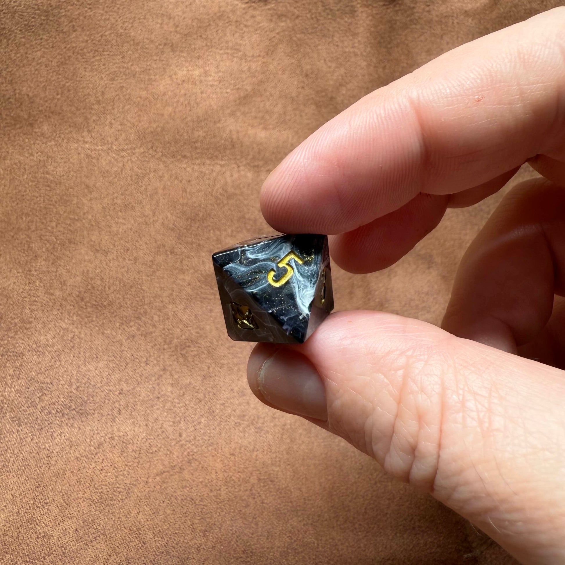Hand holding a black and white dice with yellow number '3' on a brown background