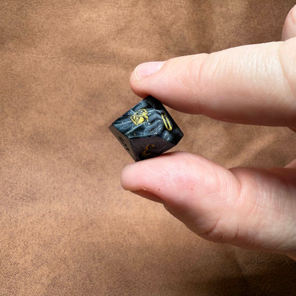 Hand holding a small black die with yellow text on a brown background