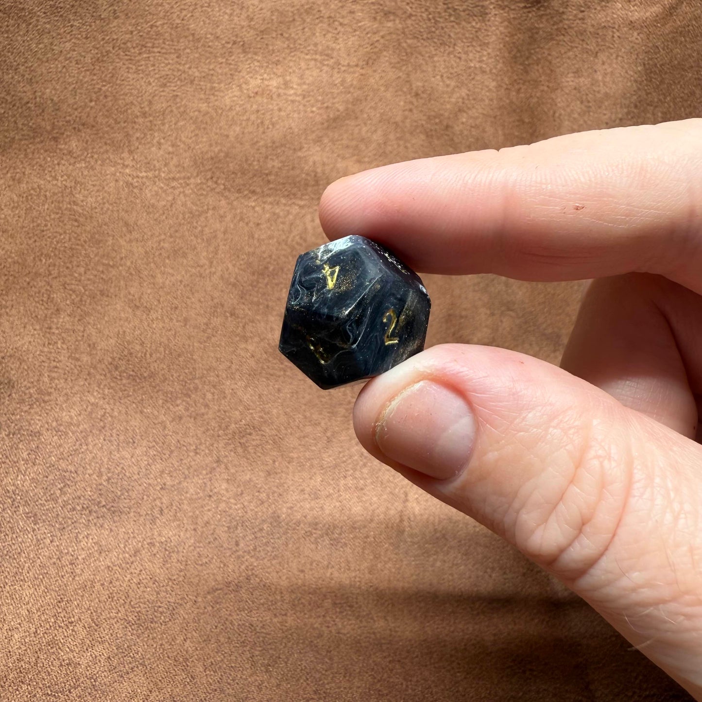 Hand holding a black crystal with gold numbers against a brown background