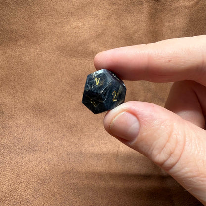 Hand holding a black crystal with gold numbers against a brown background