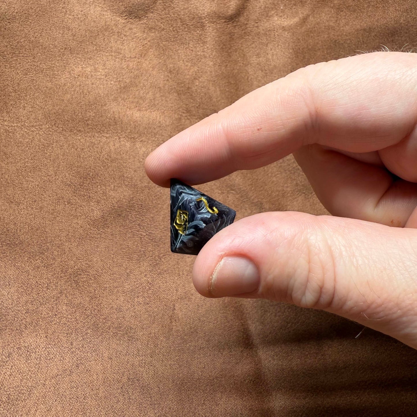 Hand holding a small black object against a brown background