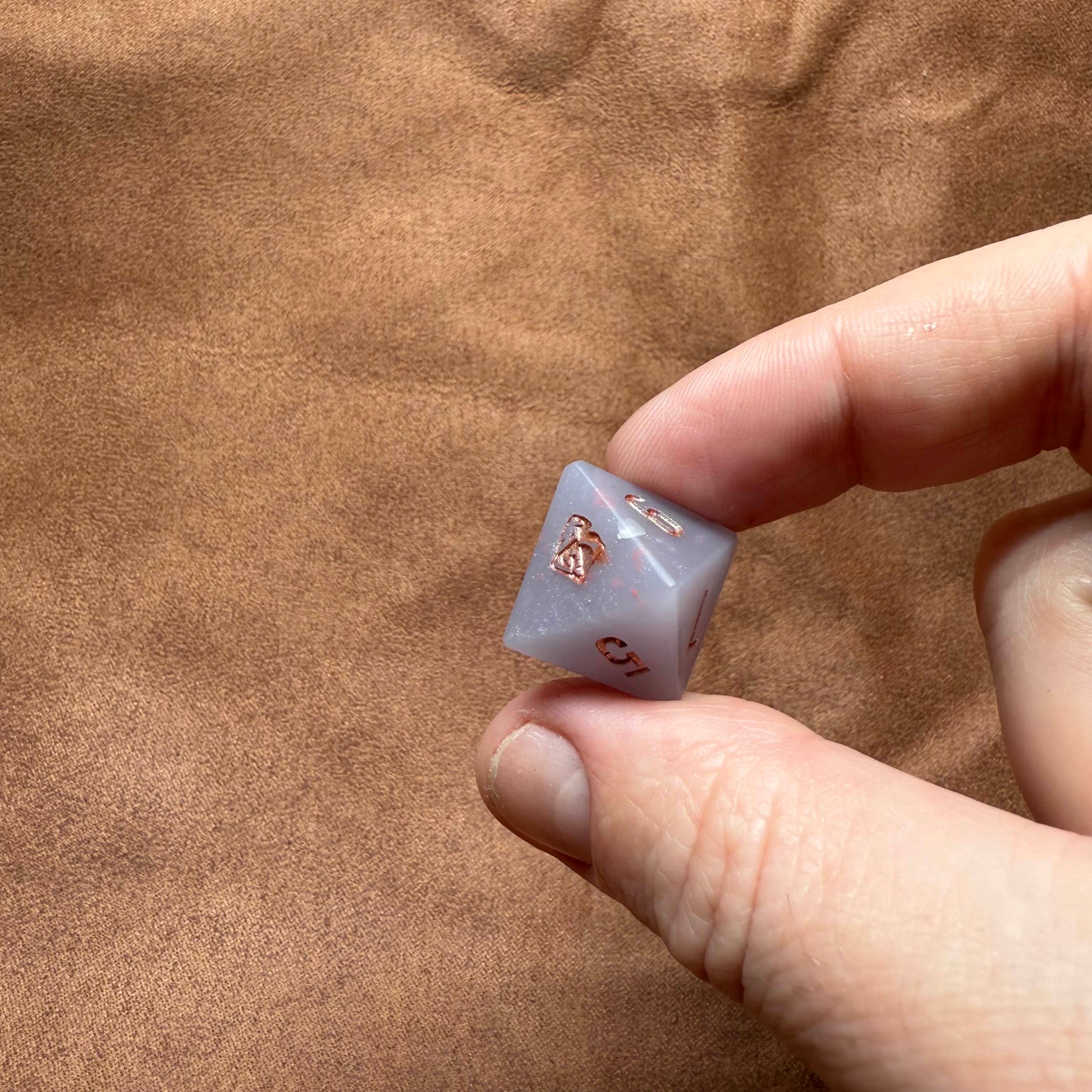Hand holding a small dice with a design on a brown surface
