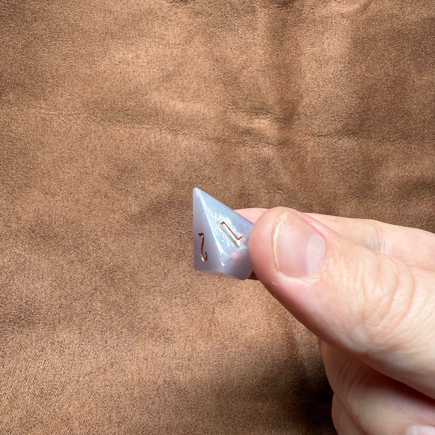 Clear plastic triangle with a small metal component held between fingers against a brown fabric background