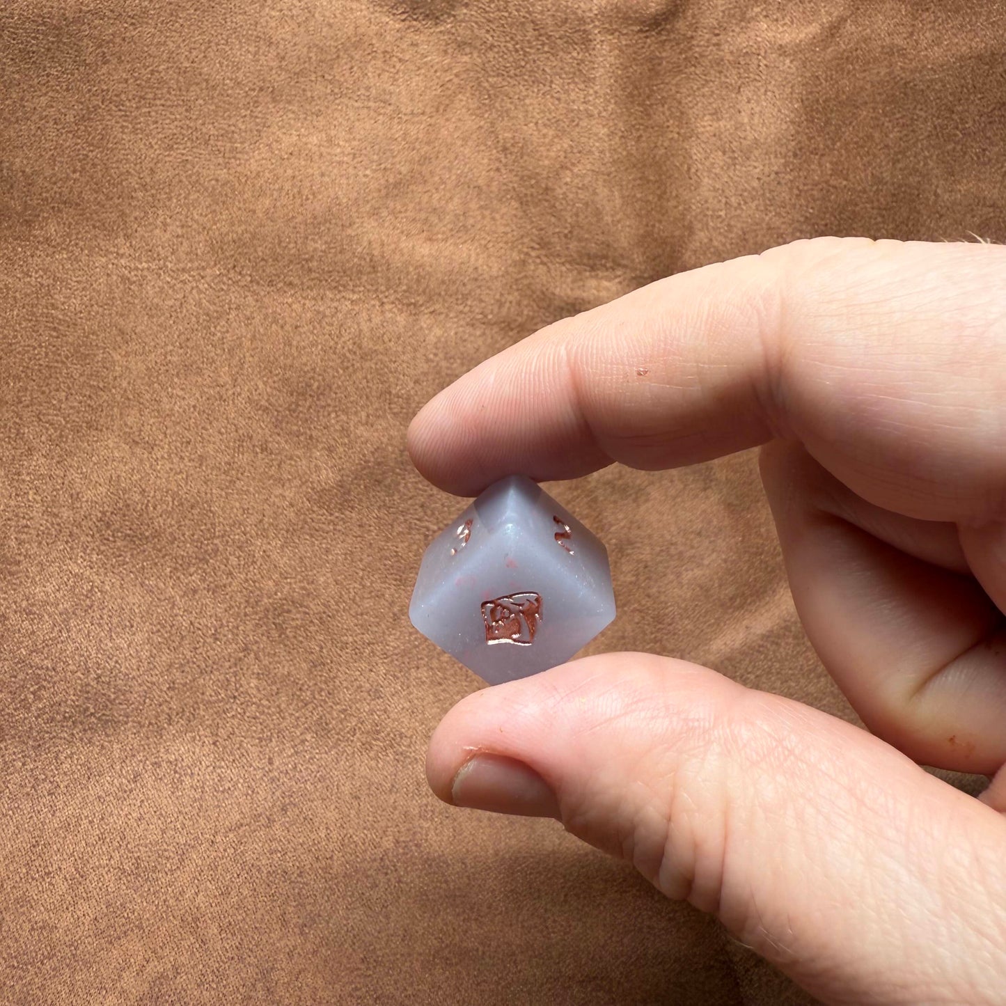 Hand holding a small translucent object against a brown fabric background