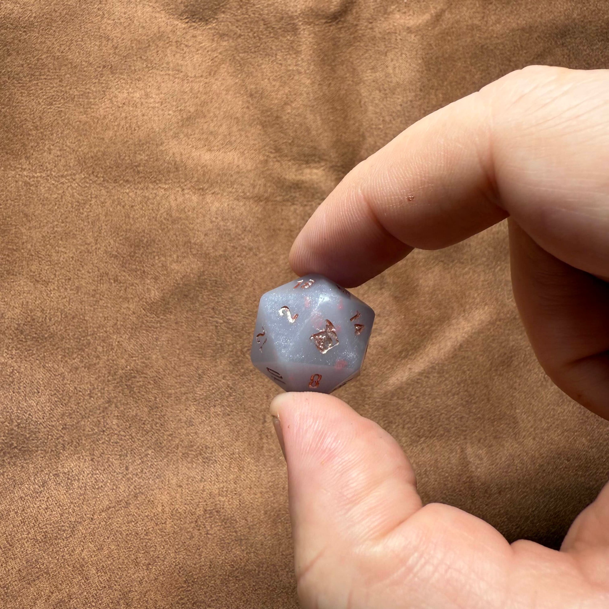 Hand holding a small blue crystal with star patterns against a brown fabric background