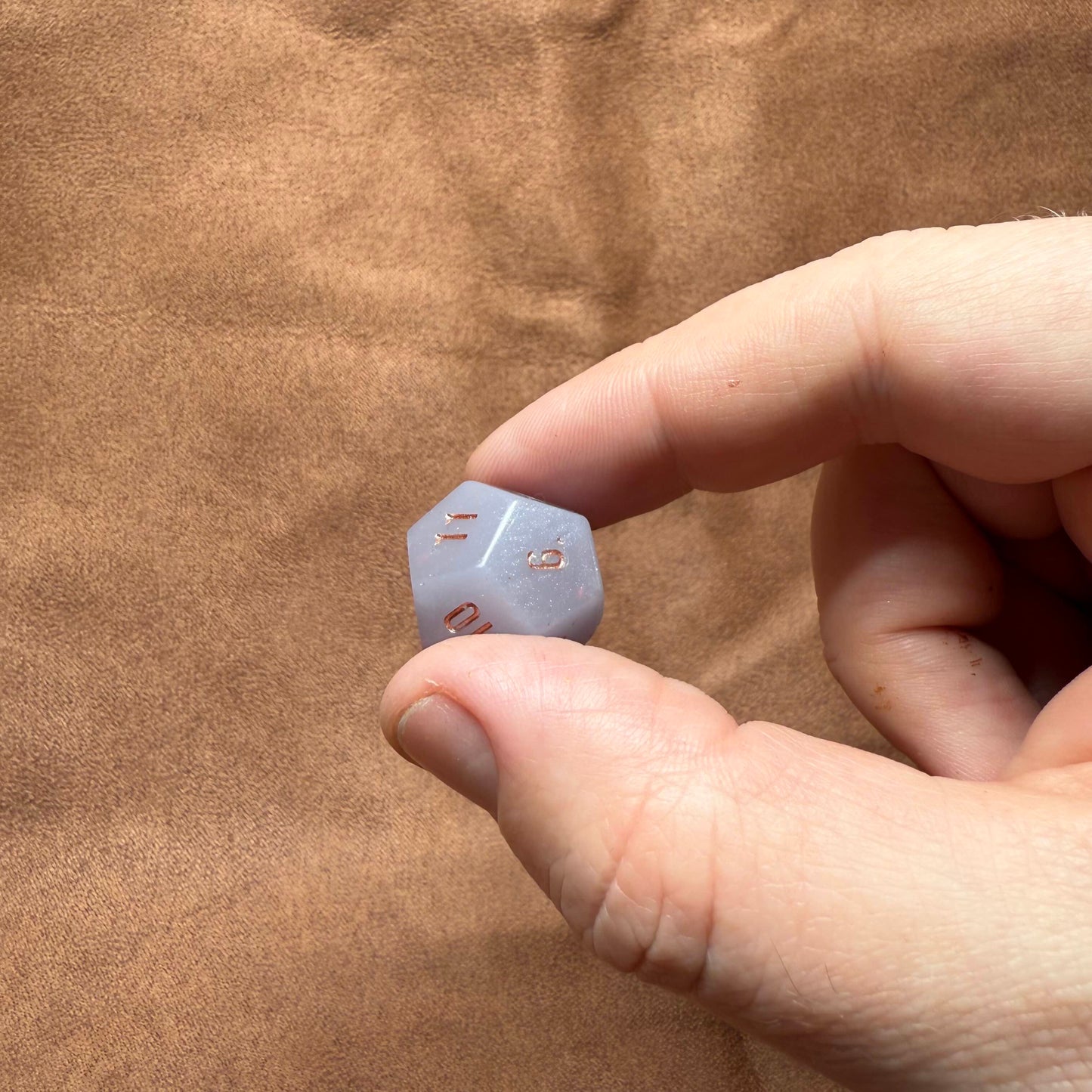 Hand holding a small blue die against a brown fabric background