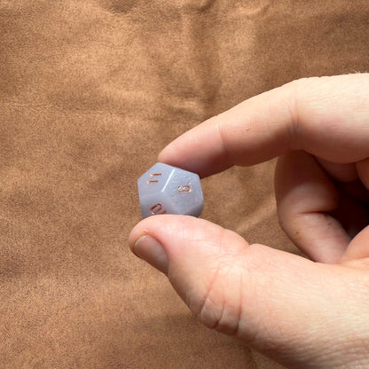 Hand holding a small blue die against a brown fabric background