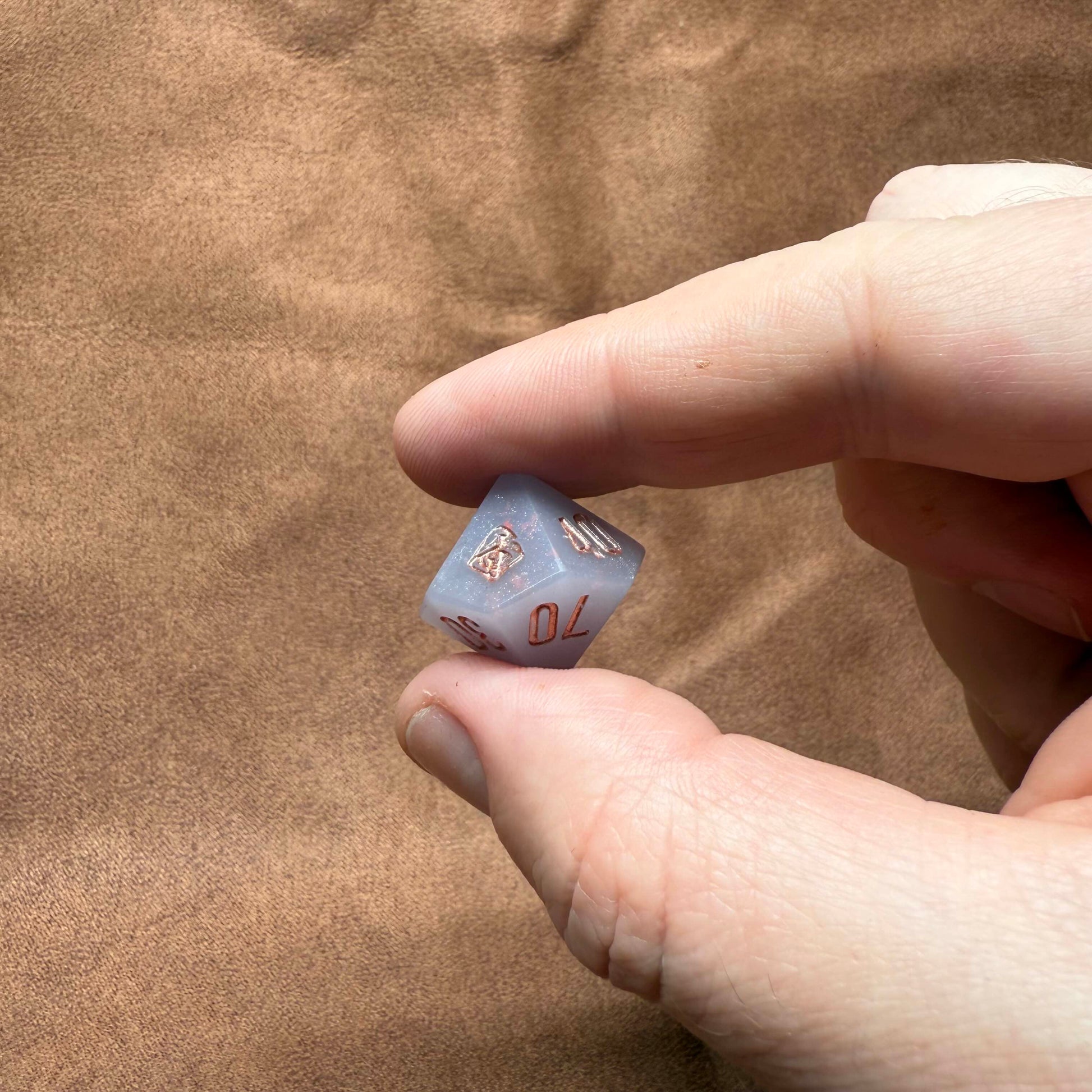 Hand holding a blue polyhedral dice with numbers on a brown textured background