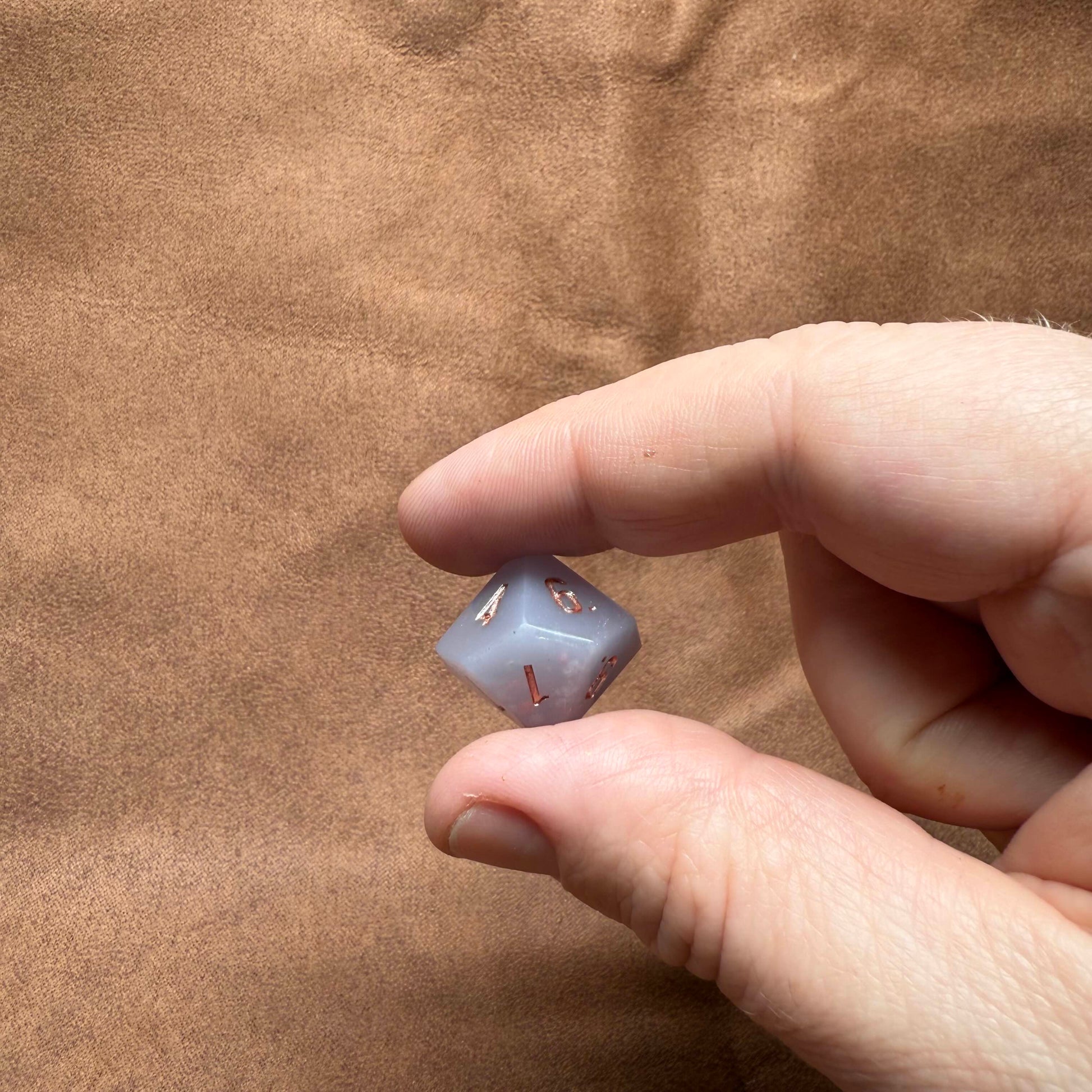 Hand holding a small die against a brown background