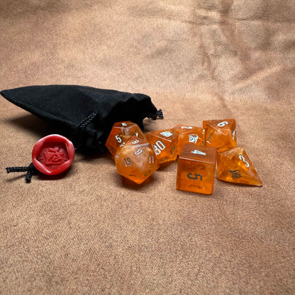 Set of amber-colored polyhedral dice with a black drawstring bag on a beige surface