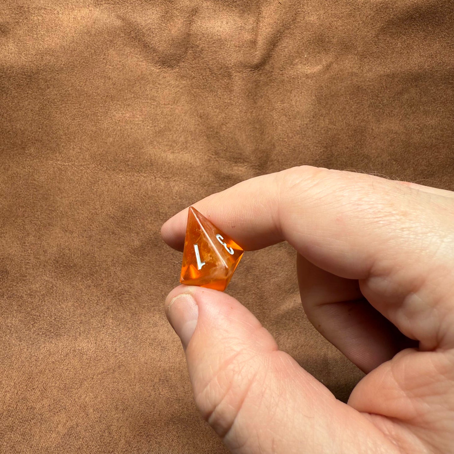 Hand holding a transparent orange die with numbers on a brown textured background