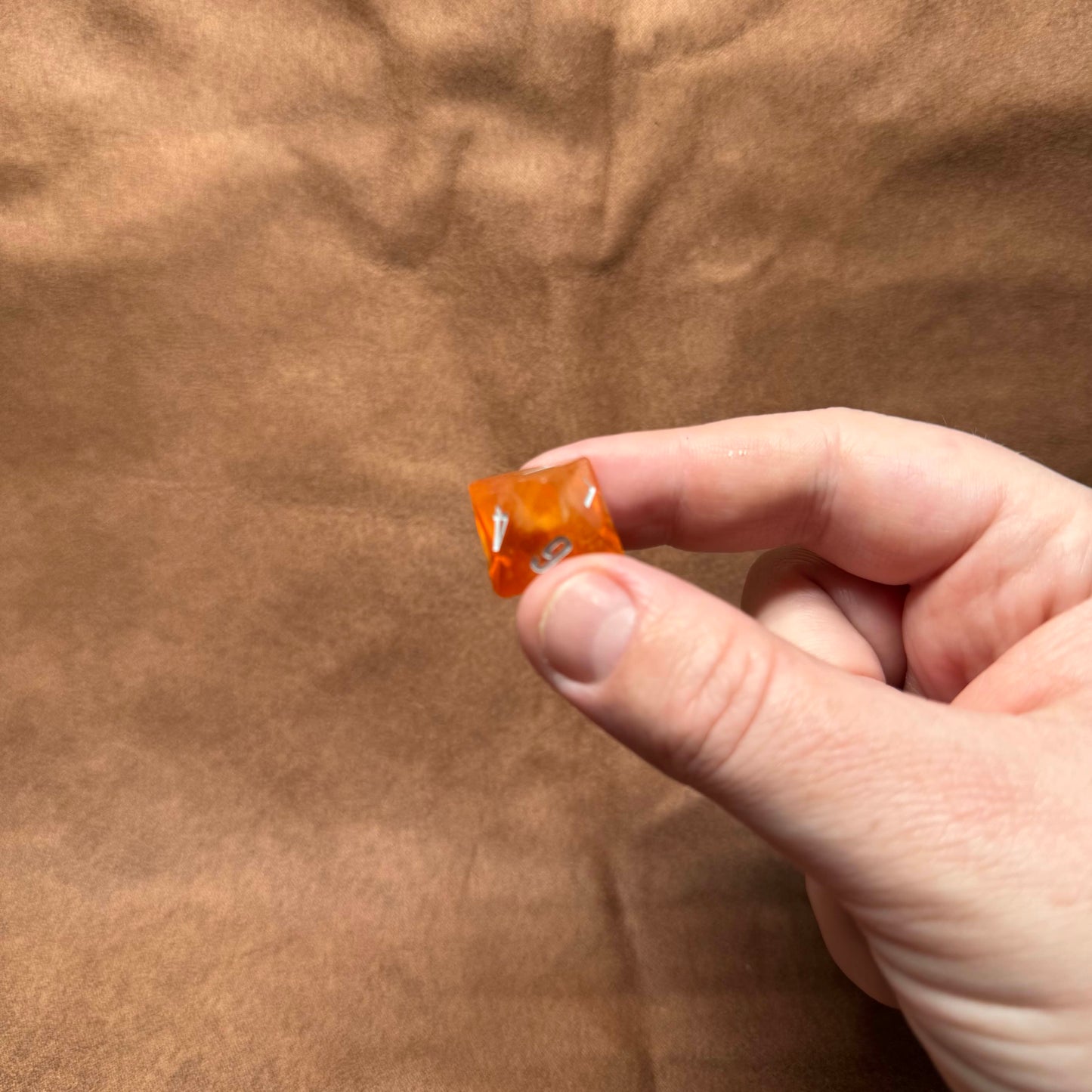 Hand holding a small orange object against a brown background