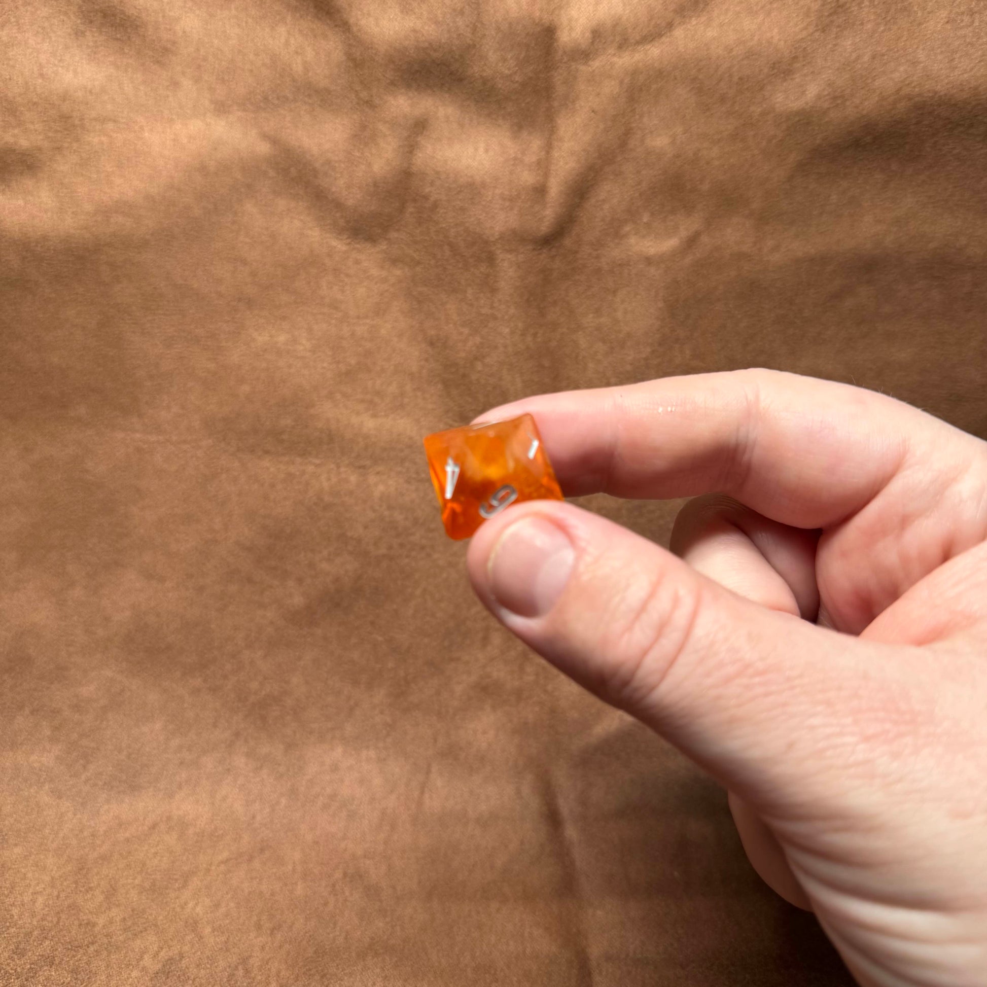 Hand holding a small orange object against a brown background