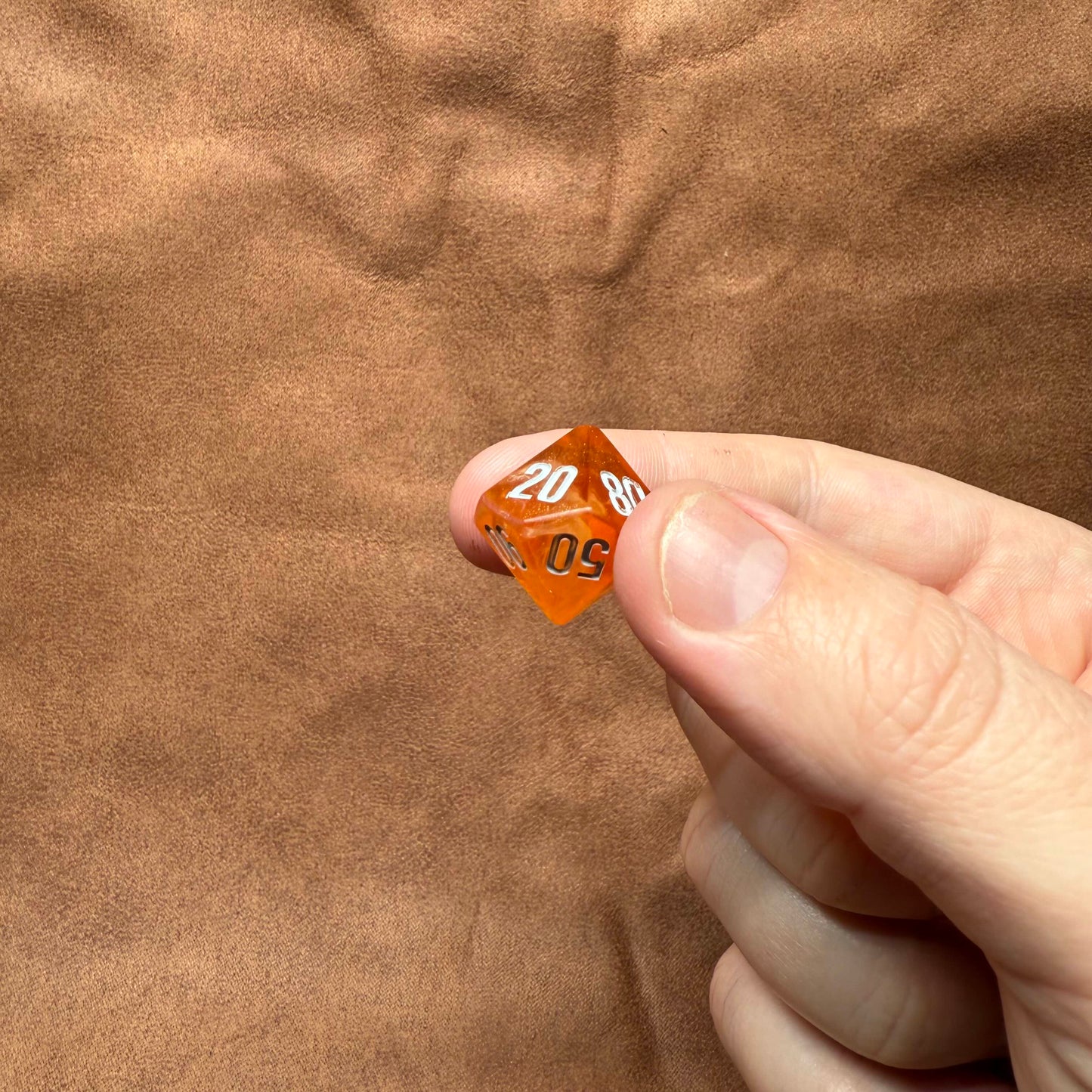 Hand holding a polyhedral dice with numbers on a brown textured background