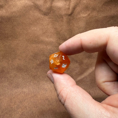 Hand holding a small orange die with numbers on a brown textured background